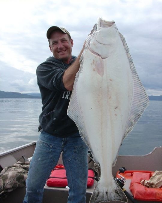 Guide holding up a bright white-belly halibut on the boat